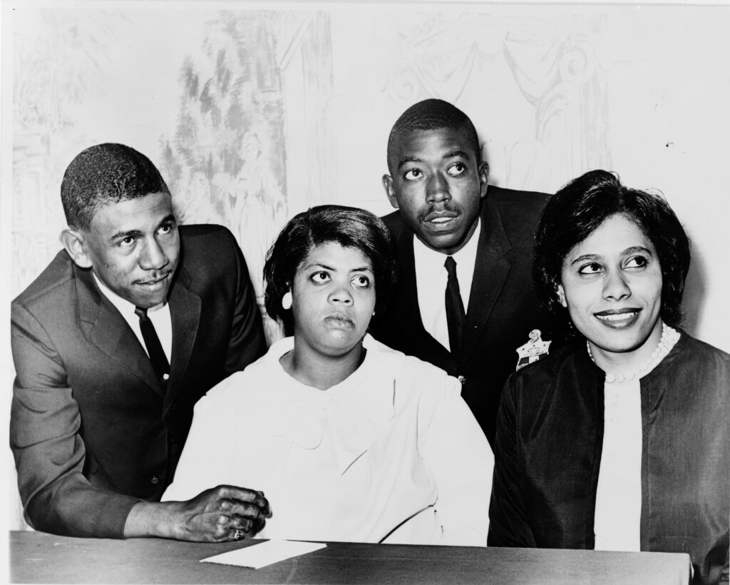 Black and white photo of Linda Brown Smith, Ethel Louise Belton Brown, Harry Briggs, Jr., and Spottswood Bolling, Jr. during press conference at Hotel Americana in 1964. Courtesy Library of Congress