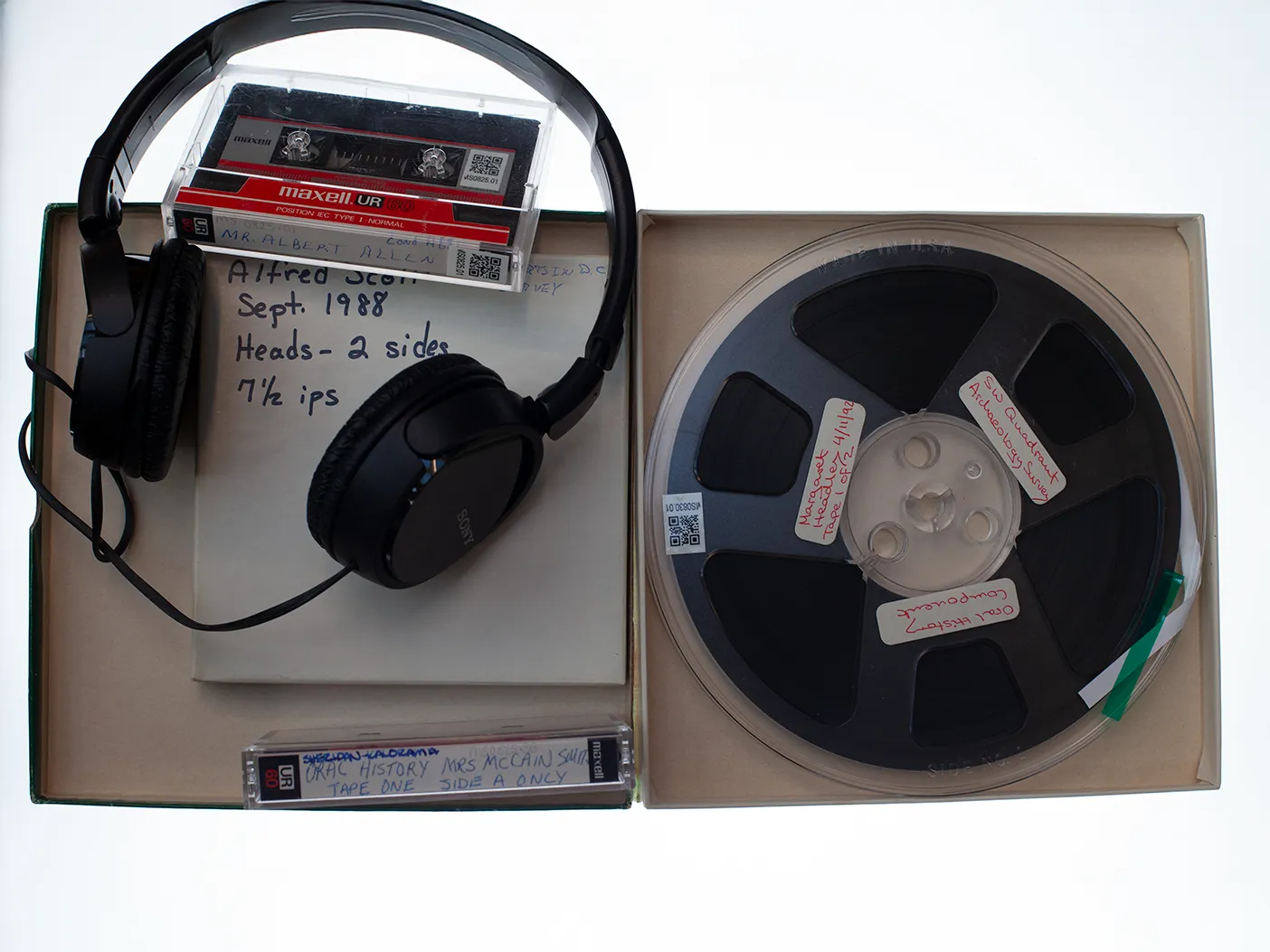 An open box with one tape, two cassette tapes, and pair of headphones. One cassette tape is labeled "Mr. Albert Allen" and the other is labeled "Oral History Mrs McCain (unintelligible) Tape One Side A Only".