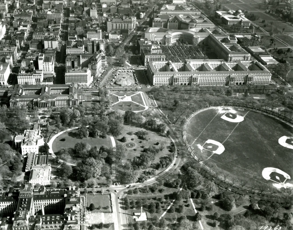 A black an white photograph shows aerial view east from 17th Street NW over the White House grounds across Pennsylvania Avenue.