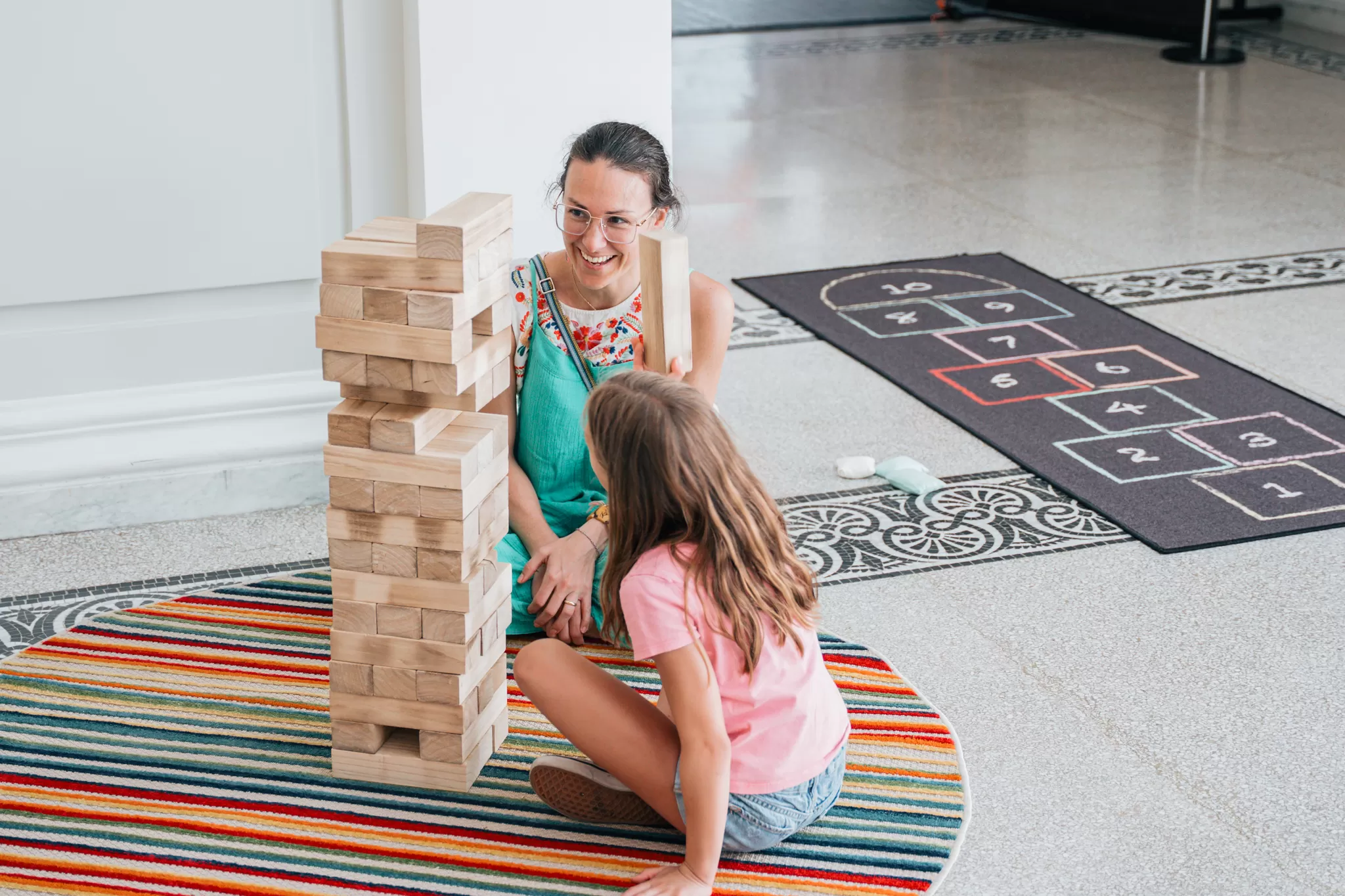Mother and daughter play giant Jenga on a colorful striped rug.